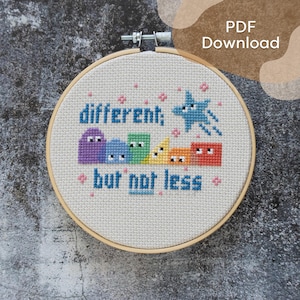 May include: A cross-stitch embroidery hoop with the words "different; but not less" in blue. The design includes colorful shapes and a blue star. The text "PDF Download" is in the upper right corner.