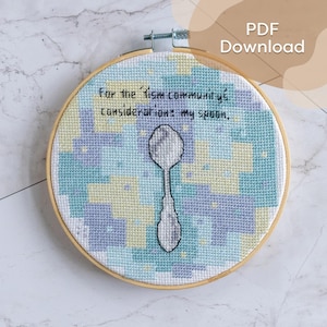 Könnte beinhalten: Kreuzstich-Stickerei in einem Holzreifen. Das Design zeigt einen Löffel in der Mitte, umgeben von einem geometrischen Muster in Blau-, Gelb- und Lilatönen. Der Text lautet: "For the 'ism community's consideration: my spoon."