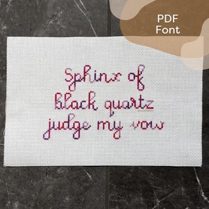 May include: Cross-stitch embroidery on white fabric with the text "Sphinx of black quartz, judge my vow".