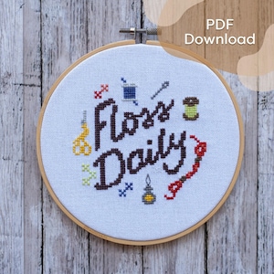 以下が含まれることがあります： 茶色の糸で「Floss Daily」という言葉が刺繍されたクロスステッチの刺繍枠。デザインには、ハサミ、針、糸巻き、その他の縫製関連アイテムのカラフルなクロスステッチ画像が含まれています。「PDF Download」という文字が右上隅にあります。