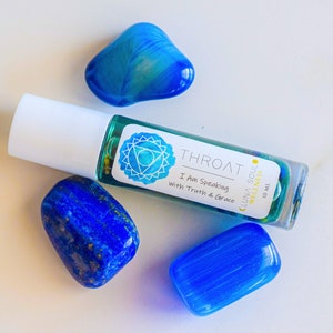 May include: A blue glass roller bottle with a white label that says "Throat I Am Speaking with Truth & Grace Luna Soul Wellness 10 ml". The bottle is surrounded by three blue stones.