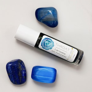 May include: A blue glass roller bottle with a label that says "Throat - I Am Speaking with Truth & Grace - CLUNA SOUL WELLNESS - 10 mL". The bottle is sitting on a white surface with three blue stones.