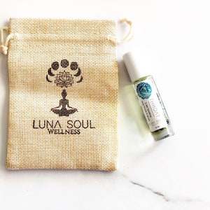 May include: A small, brown burlap pouch with the text "Luna Soul Wellness" and a stylised image of a person meditating. A small, clear glass bottle with a white label that reads "Throat" and "Luna Soul Wellness" is next to the pouch.