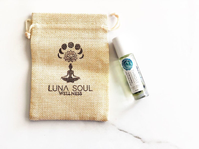May include: A small, brown burlap pouch with the text "Luna Soul Wellness" and a stylised image of a person meditating. A small, clear glass bottle with a white label that reads "Throat" and "Luna Soul Wellness" is next to the pouch.