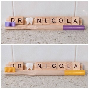 May include: A wooden toothbrush holder with a purple and yellow toothbrush, a white tooth, and the letters "DR. NICO. L. A" spelled out with wooden letter tiles.