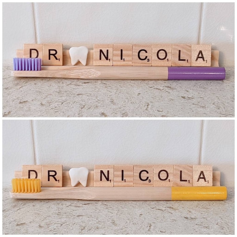 May include: A wooden toothbrush holder with a purple and yellow toothbrush, a white tooth, and the letters "DR. NICO. L. A" spelled out with wooden letter tiles.