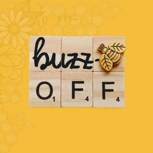 Può includere: Tessere di legno con lettere che compongono la scritta "buzz off" con un ciondolo a forma di ape dorata sulla "z".