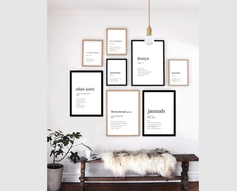 May include: A white wall with a collection of framed prints featuring Arabic words and their definitions. The prints are in black and white and have a minimalist aesthetic. A wooden bench with a white sheepskin throw sits in front of the wall.