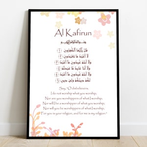 May include: A printable Islamic art print with a white background and floral accents. The print features the Arabic text of the Quranic chapter Al-Kafirun, with an English translation below. The text is in brown and the flowers are in shades of pink, orange, and yellow.