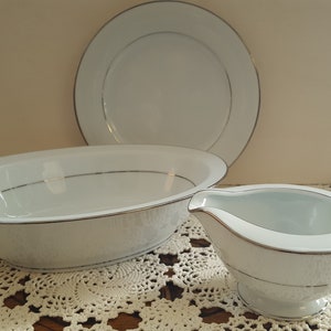Puede incluir: Un juego de tres platos de porcelana blanca con ribete plateado. El juego incluye un tazón ovalado grande para servir, un tazón redondo más pequeño para servir y una salsera.