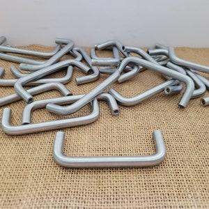 May include: A pile of silver metal drawer pulls with a rounded, u-shaped design. The pulls are arranged on a brown burlap surface.