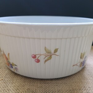 May include: White, ribbed ceramic bowl with fruit illustrations. The bowl features a wide, rounded shape with a slightly flared rim. The fruit illustrations include cherries, grapes, and other fruits. The bowl is suitable for serving or display.