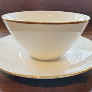 Può includere: Una salsiera in porcellana bianca con un bordo dorato, appoggiata su un sottopiatto abbinato con un bordo dorato.