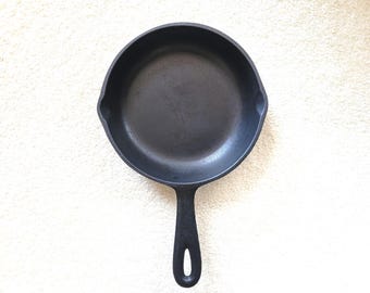 May include: A black cast iron skillet with a long handle and a rounded cooking surface. The skillet is made of heavy-duty metal and is designed for cooking on a stovetop or in an oven. The skillet measures approximately 10 inches in diameter.