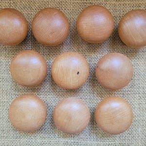 May include: Ten smooth, round, light brown wooden knobs arranged in three rows. Each knob features a natural wood grain pattern with a polished finish. The objects are spherical in shape and uniform in size, displaying a consistent light tan color.