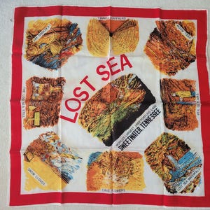 May include: A white square scarf with a red border featuring illustrations of a cave system. The scarf has the words "LOST SEA" in large red letters, and the text "WORLD'S LARGEST UNDERGROUND LAKE SWEETWATER, TENNESSEE".
