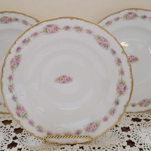Puede incluir: Tres cuencos de sopa de porcelana blanca con borde dorado y diseño floral rosa y morado.