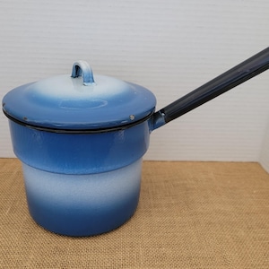 May include: A blue and white enamel saucepan with a lid and a long black handle. The pot has a gradient color scheme, transitioning from a deep blue at the base to white at the top. The handle is approximately 12 inches long.