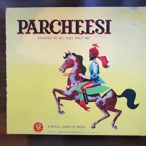 May include: A yellow box with the words "PARCHEESI" in red and black letters. The box has a picture of a man in a turban riding a white and brown horse. The text on the box reads "ENJOYED BY ALL AGES SINCE 1867" and "A ROYAL GAME OF INDIA".