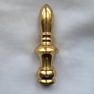 May include: A golden, decorative finial with a bulbous base and a tapered, elongated top. The finial has a series of rounded and ridged sections, creating a detailed and ornate design. The object is made of a shiny, reflective material.