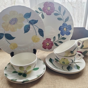 Könnte beinhalten: Ein Set vintage floral Porzellan Teetassen und Untertassen mit einem gelben, blauen und roten floralen Muster. Das Set enthält einen größeren Teller mit einem ähnlichen floralen Design.