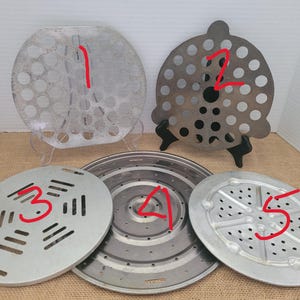 May include: Five different metal kitchen strainers are displayed. The strainers are various shapes and sizes, with perforated or slotted designs. The colors are silver and gray. The strainers are likely used for draining liquids or straining food items.