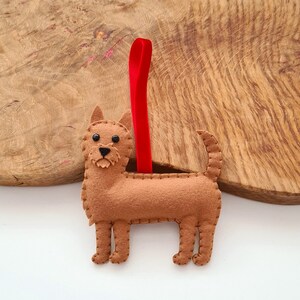 May include: A brown felt dog ornament with black eyes and a red ribbon for hanging.