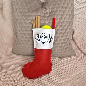 May include: Red and white felt Christmas stocking with a Dalmatian dog face appliqu&eacute;. The stocking is filled with a tennis ball and dog chew sticks.