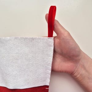 May include: A white felt Christmas stocking with a red velvet cuff and a red velvet loop for hanging.