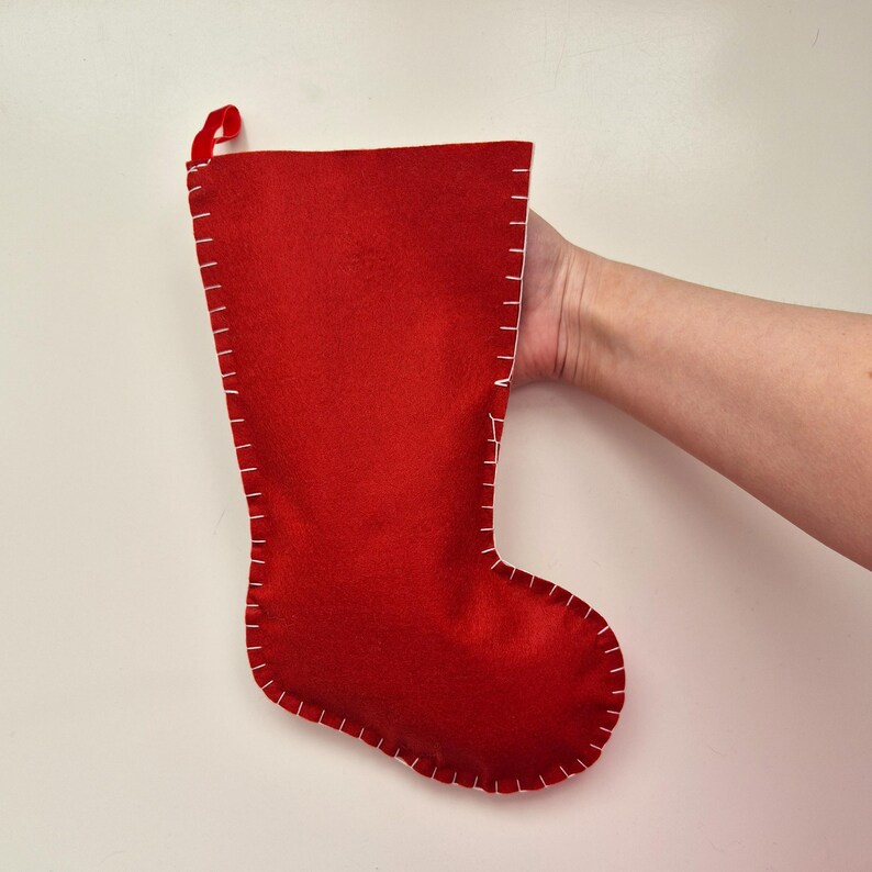 May include: A red felt Christmas stocking with white stitching around the edges. The stocking has a loop at the top for hanging.