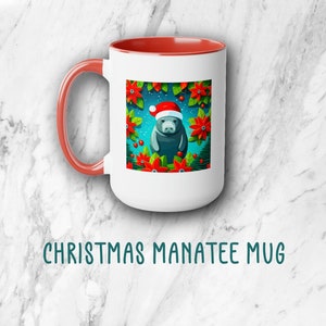 May include: White ceramic mug with a red rim and handle. The mug features a colourful illustration of a manatee wearing a Santa hat surrounded by poinsettia flowers and holly berries. The text "CHRISTMAS MANATEE MUG" is printed below the mug.