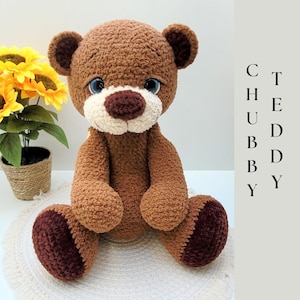 Könnte beinhalten: Ein handgefertigter brauner Teddybär mit weißer Schnauze und blauen Augen. Der Bär sitzt auf einer weißen Oberfläche mit dem Text "CHUBBY TEDDY" in Schwarz. Der Bär hat dunkelbraune Akzente an Ohren und Füßen.