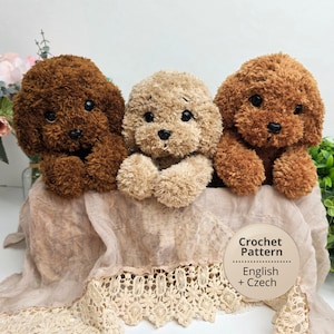May include: Three plush dog toys made of fuzzy yarn, featuring two dark brown dogs and one light beige dog in the center. Each toy has black plastic eyes and a black nose. A circular label reads Crochet Pattern English + Czech.