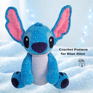 May include: A blue crocheted alien plush toy with large ears, a purple nose, and black eyes. The text "Crochet Pattern for Blue Alien" is visible. The toy is sitting on a light blue, textured surface.