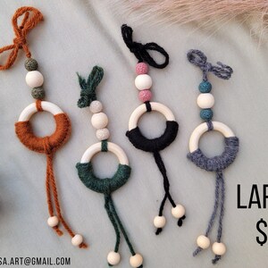 Puede incluir: Cuatro juguetes de madera en forma de anillo con hilo de lana de diferentes colores envuelto alrededor. Cada anillo tiene tres cuentas de madera unidas a la parte inferior. Los anillos están colgados de una cuerda con un nudo en la parte superior. El texto "LARGE $8" es visible en la esquina inferior derecha de la imagen.