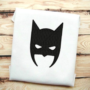 May include: Black embroidered Batman mask design on a white fabric background.