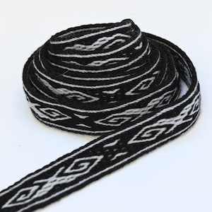 May include: Black and white woven ribbon with a geometric pattern. The ribbon is rolled up and the pattern is visible on the side.