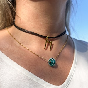 K&ouml;nnte beinhalten: Eine goldene Kettenkette mit einem gr&uuml;n-wei&szlig; gestreiften Perlenanh&auml;nger und einem goldenen Runenanh&auml;nger. Die Kette wird von einer Person mit einem wei&szlig;en Hemd getragen. Der Text "Norse Runes Wisdom by Fenrir S" ist am unteren Rand des Bildes sichtbar.