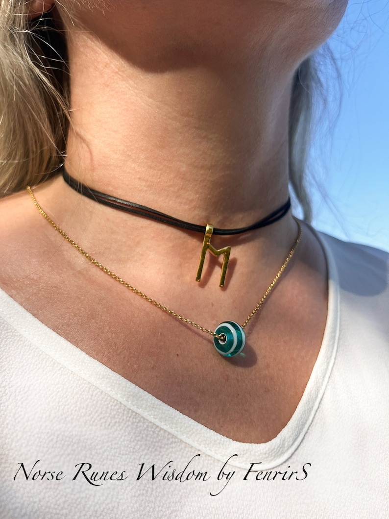 K&ouml;nnte beinhalten: Eine goldene Kettenkette mit einem gr&uuml;n-wei&szlig; gestreiften Perlenanh&auml;nger und einem goldenen Runenanh&auml;nger. Die Kette wird von einer Person mit einem wei&szlig;en Hemd getragen. Der Text "Norse Runes Wisdom by Fenrir S" ist am unteren Rand des Bildes sichtbar.