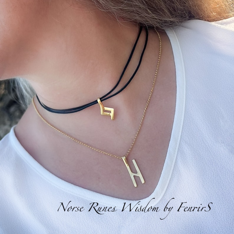 K&ouml;nnte beinhalten: Zwei goldene Halsketten mit Runenanh&auml;ngern. Die obere Halskette ist ein schwarzes Choker mit einem goldenen Runenanh&auml;nger. Die untere Halskette ist eine goldene Kette mit einem gr&ouml;&szlig;eren goldenen Runenanh&auml;nger. Der Text "Norse Runes Wisdom by FenrirS" befindet sich am unteren Rand des Bildes.