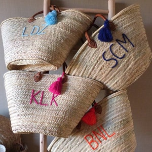 May include: Four straw tote bags with leather handles and colorful tassels. Each bag is embroidered with a different set of initials: LDZ, SCM, KLR, and BML.