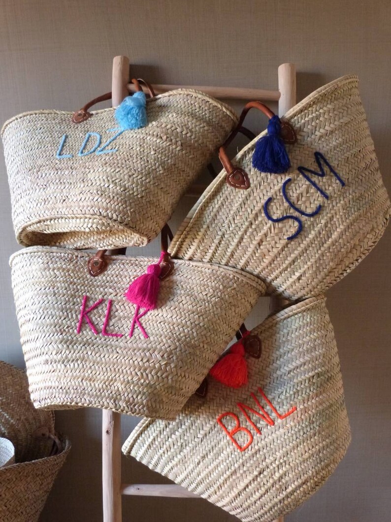 May include: Four straw tote bags with leather handles and colorful tassels. Each bag is embroidered with a different set of initials: LDZ, SCM, KLR, and BML.