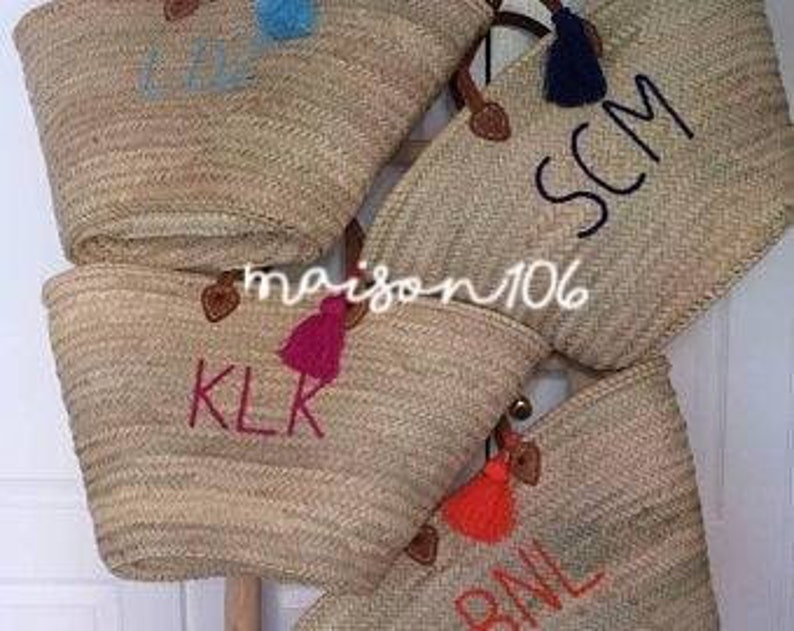 May include: Four straw tote bags with leather handles and colorful tassels. Each bag has a different name embroidered on the front: KKL, BNL, SCM, and "I Love".
