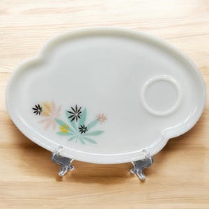 Peut inclure: Plateau de service ovale blanc avec un motif floral dans les tons de rose, vert et noir. Le plateau a une petite indentation pour une tasse ou une soucoupe.