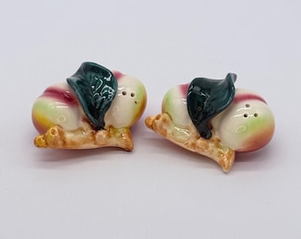 Vintage handbeschilderde keramische zout- en peperstrooiers in perzikvorm met glanzende groene bladeren.