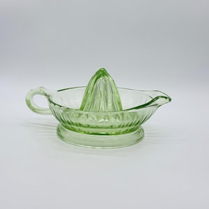 Puede incluir: Una taza de cerámica blanca con un asa negra y el texto "But First, Coffee" en negro, con una fuente de estilo manuscrito. La taza está sobre una superficie blanca.