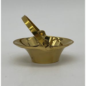 May include: A small, gold-colored metal basket with a hinged handle. The basket has a flared, rounded shape and a shiny finish. The handle is attached with a small, round fastener. The basket is likely decorative.
