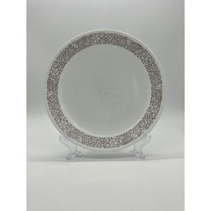 Puede incluir: Plato de cerámica blanco con un borde floral marrón. El plato es redondo y tiene un diseño simple y elegante. El patrón floral es detallado y añade un toque de sofisticación.