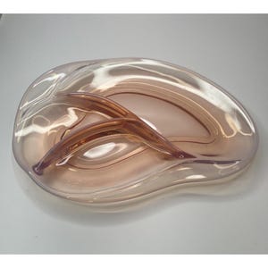 May include: A clear, oval-shaped glass serving dish with a divided design. The dish has a soft pink hue and features two curved, raised dividers. The overall design is elegant and suitable for serving appetizers or small portions.