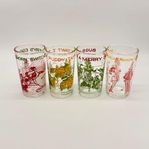 Op de afbeelding: Vier vintage drinkglazen van helder glas met cartoonkarakterontwerpen in rood, groen, geel en wit. Elk glas heeft een ander ontwerp en tekst, waaronder "HORN SWITCH", "I TWAT PUDDY TAT", "BUGS A MERRY" en "MONICA FASHION".